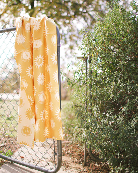 Sunny Wander & Travel Towel hanging on a fence, showcasing its vibrant sunshine design and travel-friendly size.