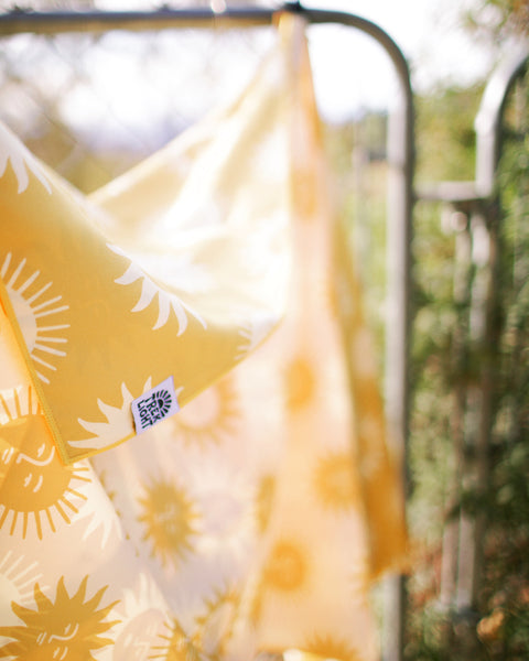 Sunny Wander & Travel Towel showcasing a vibrant sunshine design hanging outdoors.