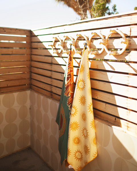 Sunny Wander & Travel Towel hanging in a sunny space, showcasing its vibrant sunshine design and practical use.
