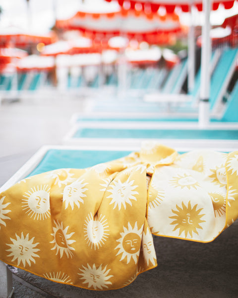 Sunny Wander & Travel Towel with vibrant sunshine design on a lounge chair by the pool.