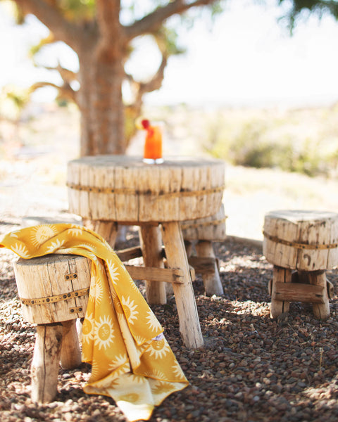 Sunny Wander & Travel Towel draped over a wooden stool in a sunny outdoor setting.