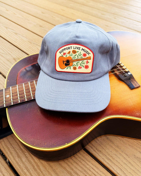 Support Live Music Hat placed on an acoustic guitar, showcasing its vibrant design and message.