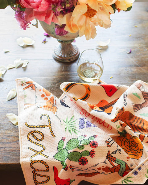 Texas Kitchen & Tea Towel featuring vibrant designs on a table with a glass of wine.