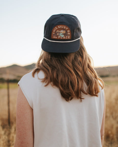 Person wearing This Must Be The Place Hat (Mountains) while enjoying a scenic outdoor view.