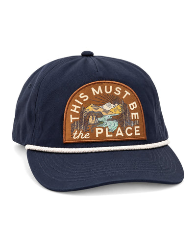 This Must Be The Place Hat in Mountains, a navy cap with white rope trim and a brown mountain and river patch, on white.