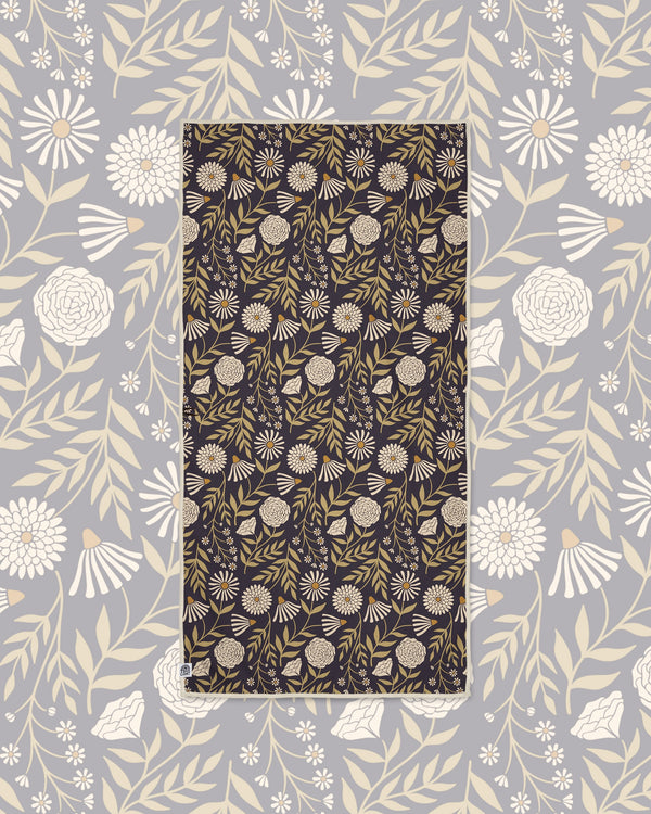 Travelin' Light Wander & Travel Towel in dark plum with cream and olive floral print, laid on a gray floral background.