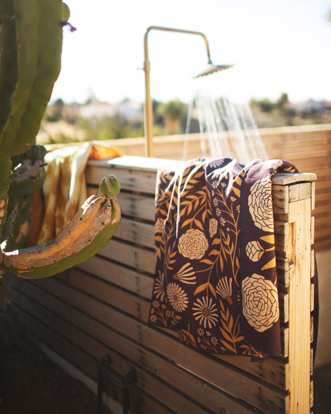Travelin' Light Wander & Travel Towel hanging near an outdoor shower, showcasing its vibrant design and functionality.