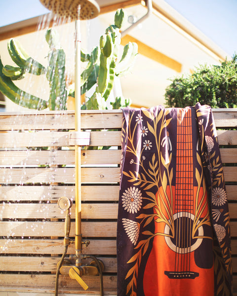 Travelin' Light Wander & Travel Towel hanging in a shower with cactus background, showcasing its vibrant design.