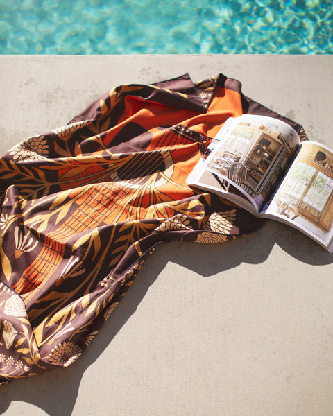 Travelin' Light Wander & Travel Towel laid by a poolside with a book, showcasing its vibrant design.