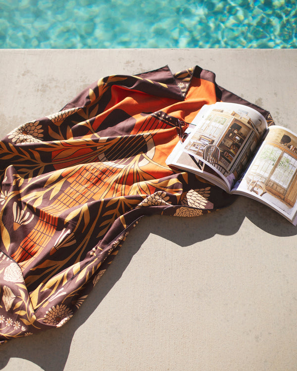 Travelin' Light Wander & Travel Towel laid by a poolside with a book, showcasing its vibrant design.