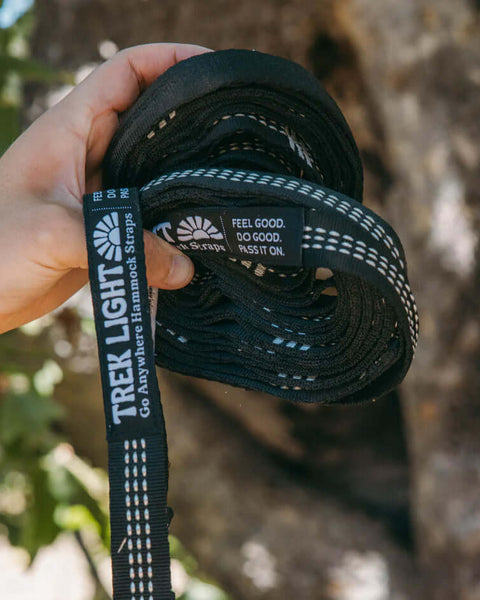 Hand holding Trek Light Go Anywhere Hammock Straps with trees in the background.