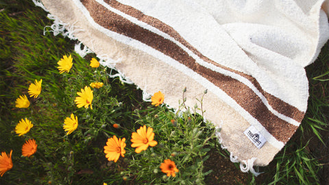Cozy blanket on grass surrounded by bright yellow flowers, perfect for relaxing outdoors.