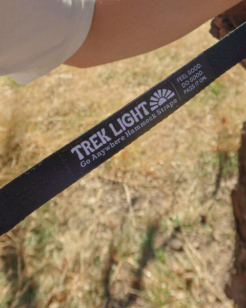 Close up of a black Go Anywhere Pro Hammock Straps webbing strap with the Trek Light logo held by a tree