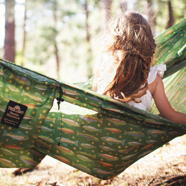 Girl relaxing in a Double Hammock & Pro Hanging Straps (River Trout Print) in a forest setting.