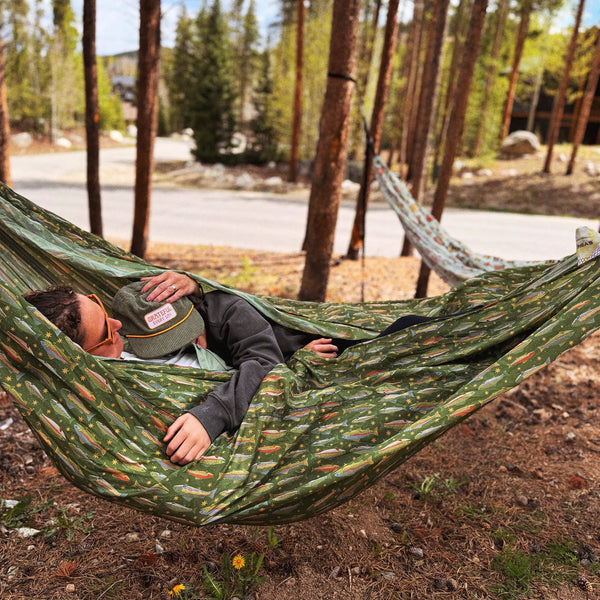 A person relaxing in a Double Hammock & Pro Hanging Straps (River Trout Print) in the woods.