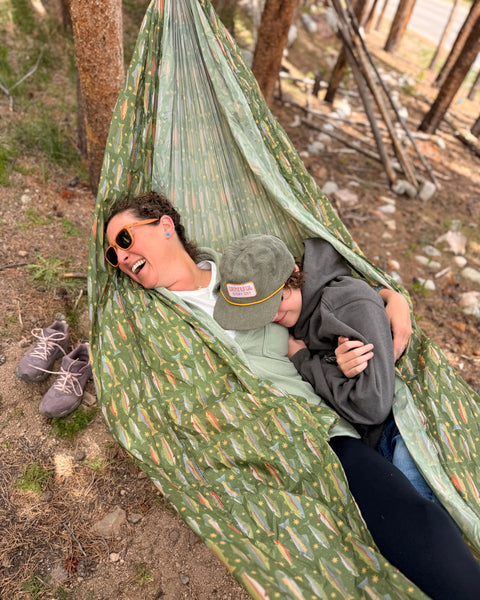 Two people relaxing in a Double Hammock & Pro Hanging Straps (River Trout Print) in a forest setting.