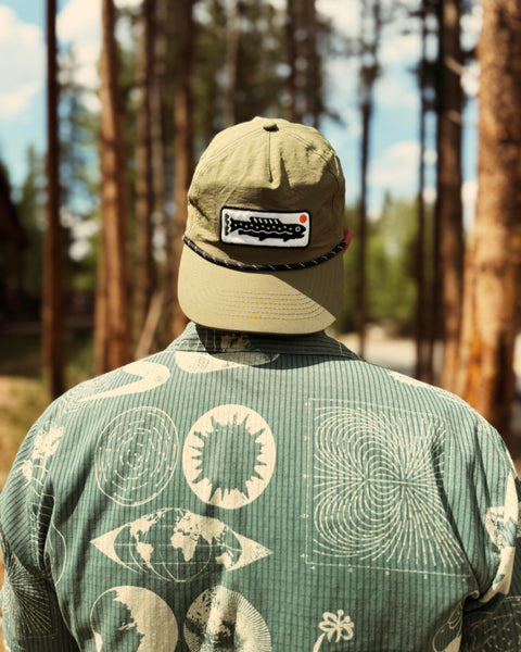 Person wearing Trout Hat (Olive) in a forest setting, showcasing its design and outdoor style.