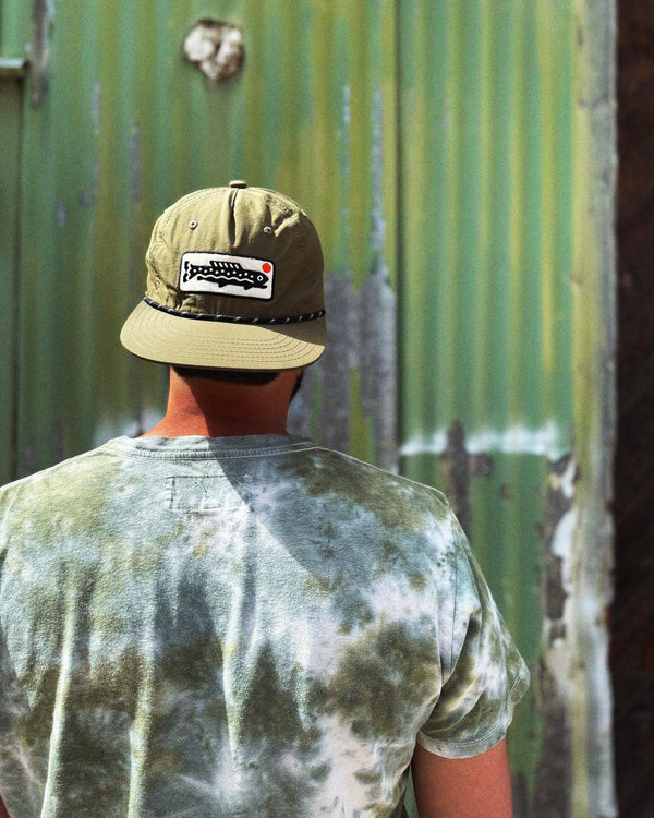 Person wearing a Trout Hat (Olive) against a rustic green backdrop, showcasing style and versatility.