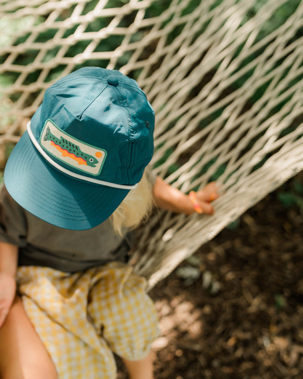 Trout Kids Hat on a child sitting in a hammock, perfect for little anglers enjoying outdoor adventures.