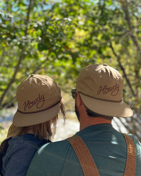 Howdy Hat Twinsie Set in tan nylon with brown script, worn by an adult and child outdoors under green trees