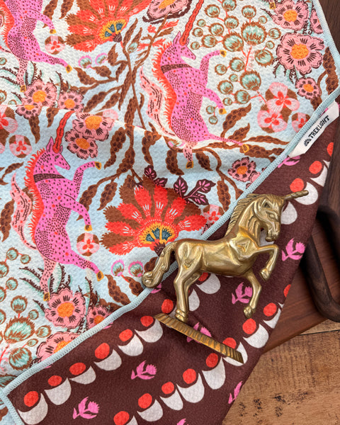 Unicorn Dreams Kitchen & Tea Towel featuring vibrant patterns and golden horse accent on wood surface.
