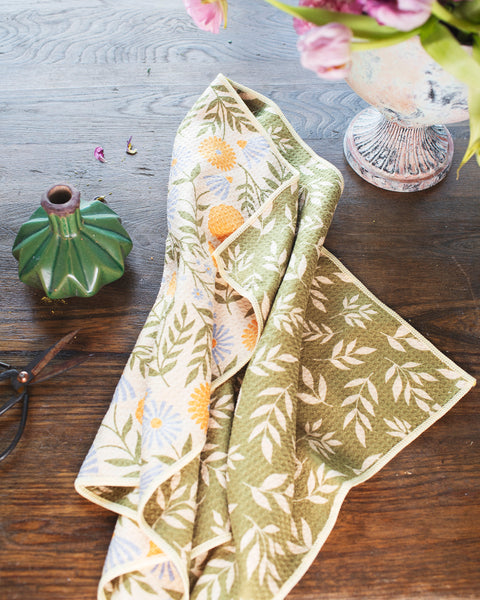 Wavy Flowers Kitchen & Tea Towel displayed on a wooden table with flowers and a vase.