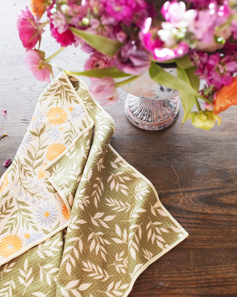 Wavy Flowers Kitchen & Tea Towel on a wooden table with a colorful flower arrangement.