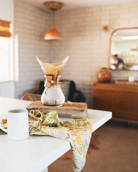 Wavy Flowers Kitchen & Tea Towel on a table with a mug, showcasing vibrant double-sided designs and eco-friendly materials.