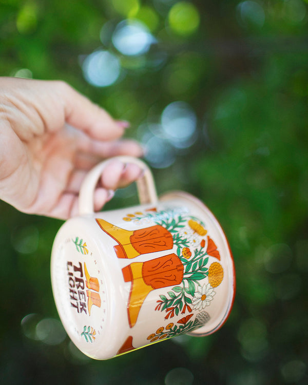 Hand holding Trek Light Western Bloom Enamel Mug 16oz with colorful floral design, perfect for outdoor adventures and happiness.
