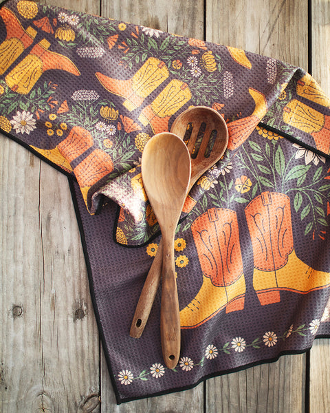 Western Bloom Kitchen & Tea Towel featuring colorful cowboy boots and wooden cooking utensils on a rustic background.