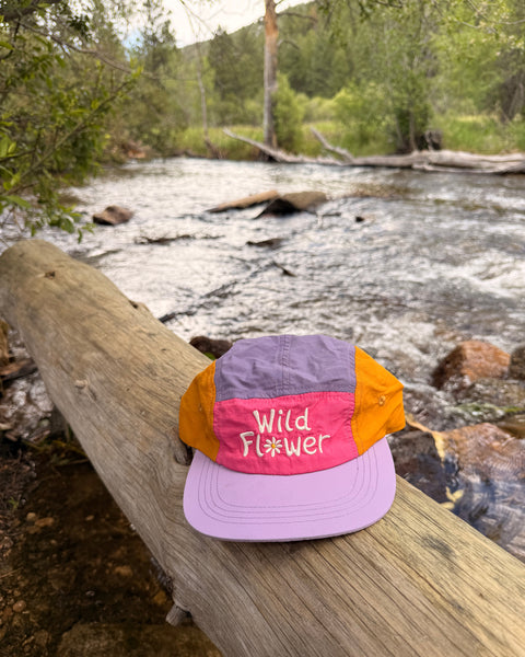 Colorful Wild Flower Kids Hat resting on a log by a river, perfect for sunny adventures.