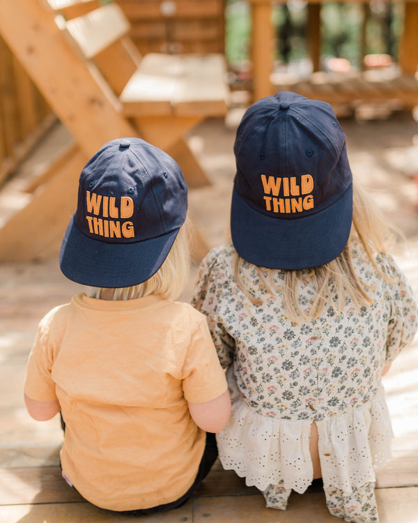 Two kids wearing Wild Thing Kids Hat, enjoying a sunny day of fun and adventure in the park.