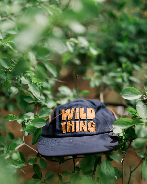 Wild Thing Kids Hat resting on green foliage, showcasing a playful design for adventurous children.
