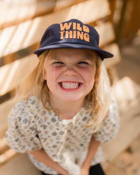 A happy child wearing a Wild Thing Kids Hat, showcasing the playful design and vibrant style ideal for outdoor fun.