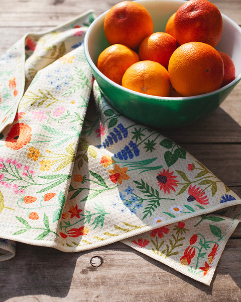 Wildflower Wonder Kitchen & Tea Towel with colorful floral design beside a bowl of oranges.