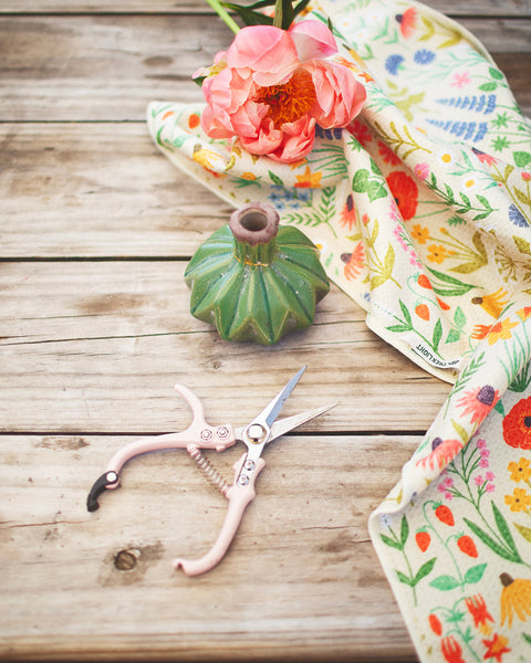 Wildflower Wonder Kitchen & Tea Towel design with pink flower, green vase, and scissors on wooden table.