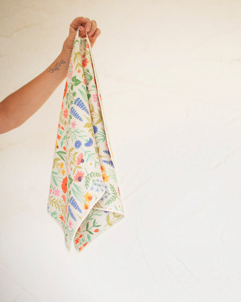 Wildflower Wonder Kitchen & Tea Towel featuring vibrant floral designs and a hand holding it for easy display.