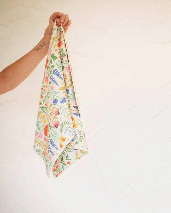 Wildflower Wonder Kitchen & Tea Towel featuring vibrant floral designs and a hand holding it for easy display.