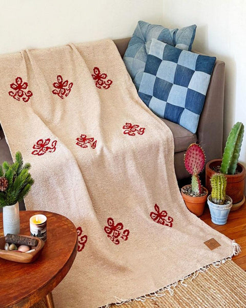 Cozy living room with a Trek Light blanket draped over a sofa, surrounded by cacti and a checkered pillow. Perfect for relaxation.