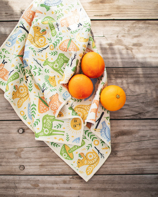 Woodland Friends Kitchen & Tea Towel with vibrant forest designs on wooden table with oranges, eco-friendly and super absorbent.