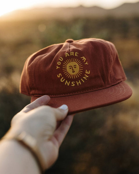 You Are My Sunshine Hat held in hand with sunset background, showcasing the sunny design and 5-panel style.