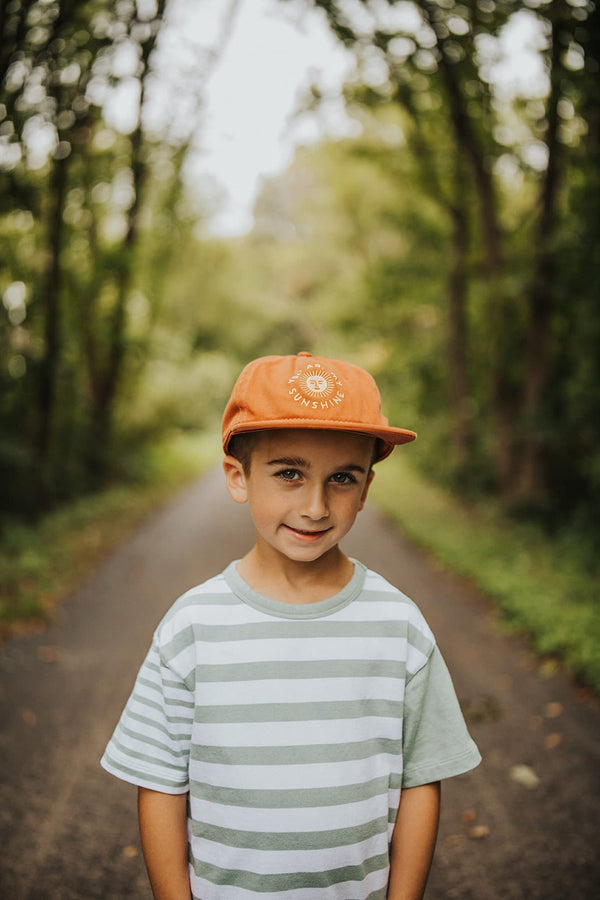 Child wearing matching orange 'You Are My Sunshine' hat on a nature path; part of the Twinsie set for adults and kids. By Trek Light.