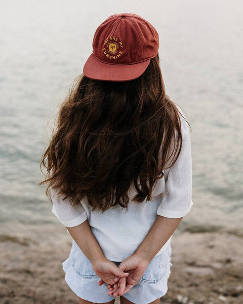 You Are My Sunshine Kids Hat worn by a child with long hair facing a tranquil body of water.