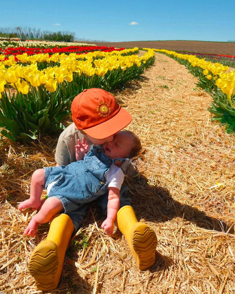 You Are My Sunshine Kids Hat worn by a toddler, playing in a field of colorful tulips.