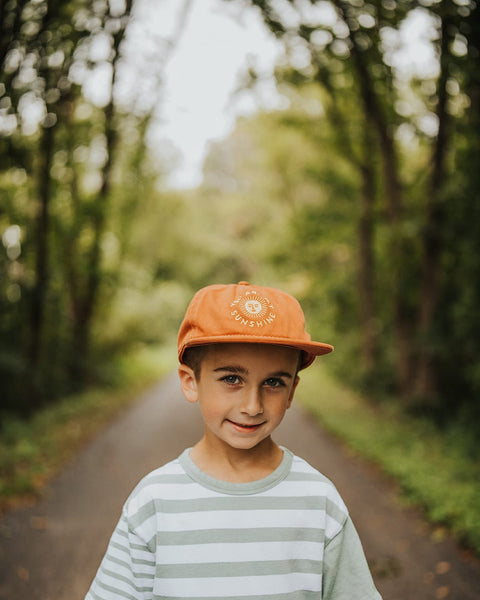 Child wearing "You Are My Sunshine" orange kids hat, standing on a forest path. Trek Light kids snapback for outdoor adventures.
