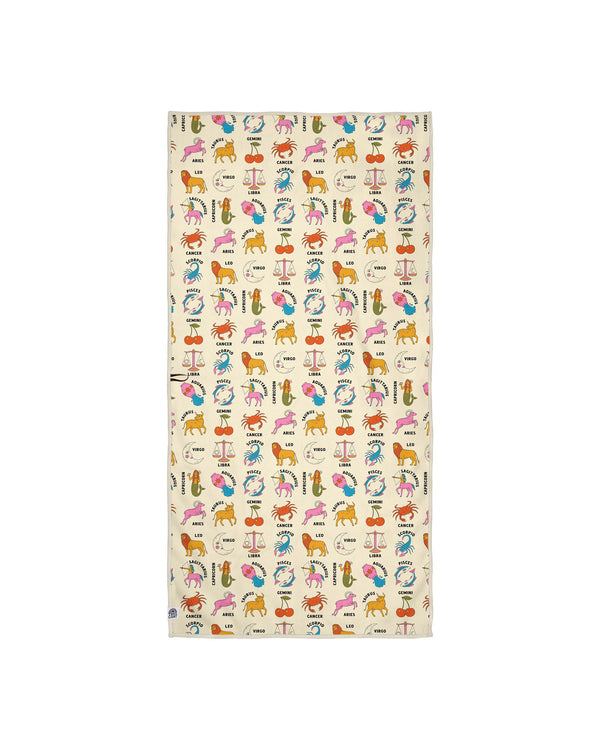 Zodiac patterned towel on cream background with scattered zodiac icons including lion, crab, scales, ram, and fish symbols in playful watercolor style