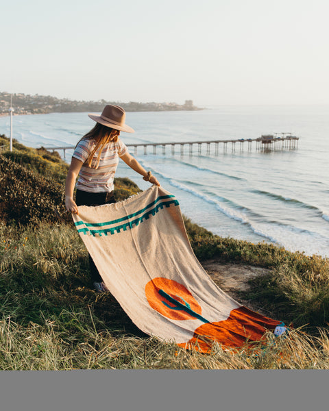 Person enjoying a cozy, versatile Arizona Blanket by the seaside; handwoven, made from recycled clothing materials, beautiful Trek Light design.