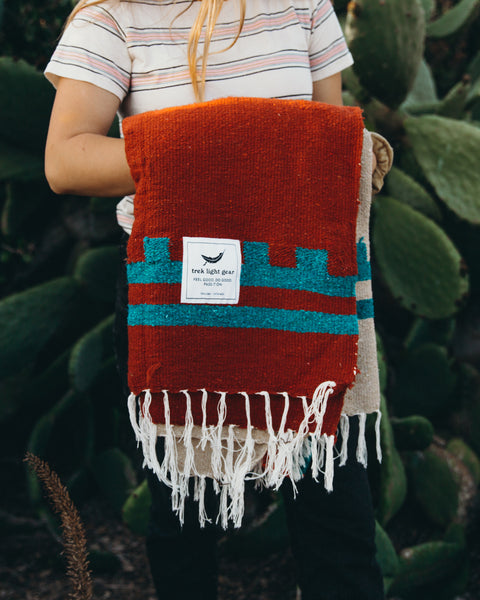 Handwoven Arizona Blanket made from recycled clothing, beautiful and cozy, perfect for versatile use by Trek Light, held in cactus backdrop.