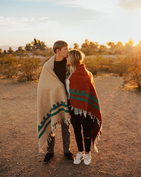 Couple wrapped in handwoven Arizona Blanket by Trek Light. Cozy and beautiful, against a Southwest sunset, made from recycled materials.