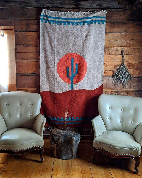 Arizona Blanket by Trek Light, handwoven from recycled clothing, draped in a cozy, rustic setting between two chairs. Beautiful and versatile design.